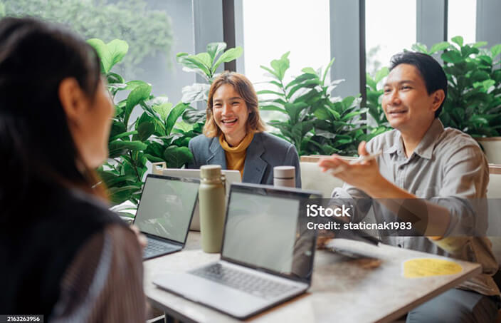 A group of workers sitting around a table talking with their laptops in front of them