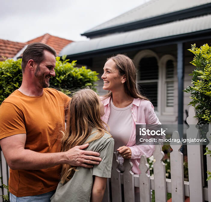 Photo of a young family smiling across their white picket fence